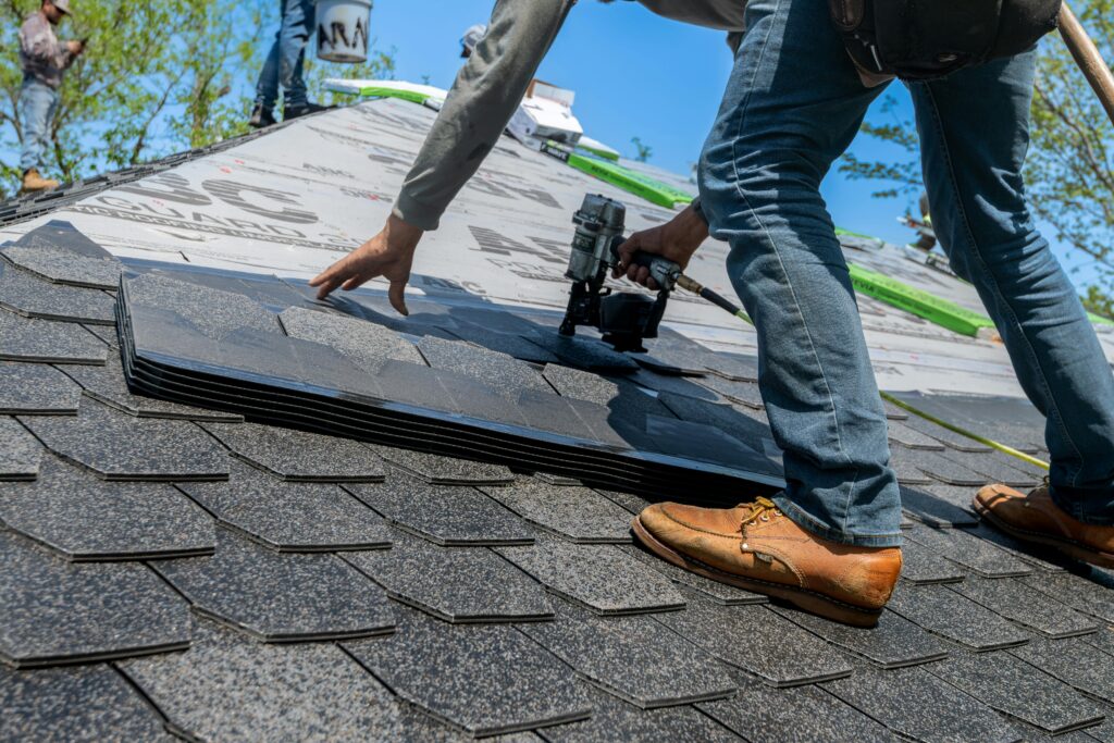 A roofer with a nail gun placing shingles on a roof.